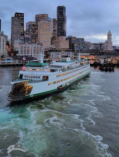 a large boat traveling down a river next to a tall cityscape in the distance