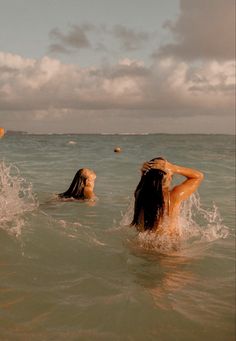 two women swimming in the ocean with one holding her hair back and another laying down