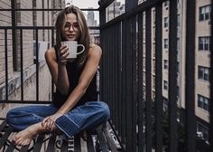 a woman sitting on top of a wooden bench holding a coffee cup