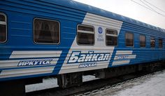 a blue and white train traveling down tracks next to snow covered ground with power lines in the background