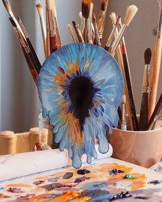 an artistically painted blue flower sitting on top of a table next to paintbrushes