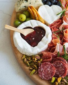 a platter filled with meats, cheese and olives on a wooden plate