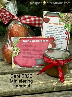 a jar of apples next to some cards on a wooden table with a red ribbon