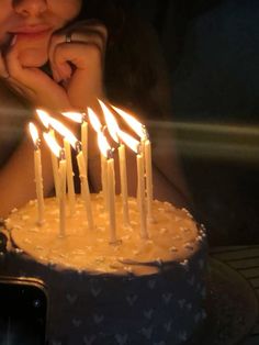 a woman sitting in front of a cake with lit candles