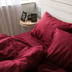 a bed with red sheets and pillows next to a night stand on the side table