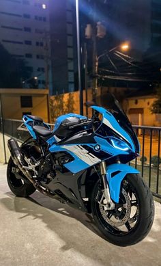 a blue and black motorcycle parked in front of a fenced area at night time