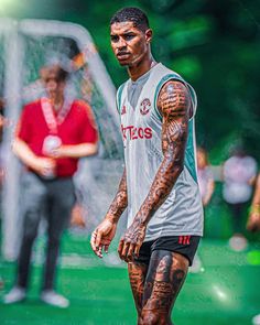 a man with tattoos on his arm and leg standing in front of a soccer ball