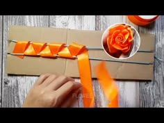 someone is making an orange rose out of paper and ribbon on a piece of cardboard