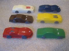 four plastic toy cars sitting on top of a table next to each other in different colors