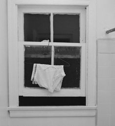 an unbuttoned shirt hanging on a window sill in a white bathroom