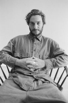 a black and white photo of a man sitting in a chair with his hands folded