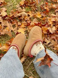 someone wearing slippers and jeans standing in the leaves