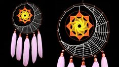 two small dream catchers with feathers hanging from them on a black background, one is orange and the other is pink