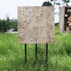 a wooden sign sitting in the grass next to a pile of firewood with holes on it