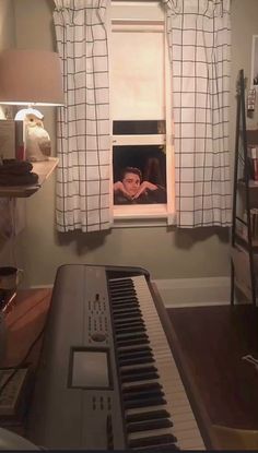 a piano in front of a window with a person peeking out