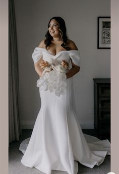 a woman in a white wedding dress standing next to a window with her hands on her hips