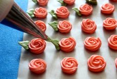 a person cutting red icing on to small roses