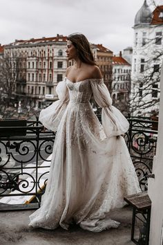 a woman in a white wedding dress standing on a balcony looking off into the distance