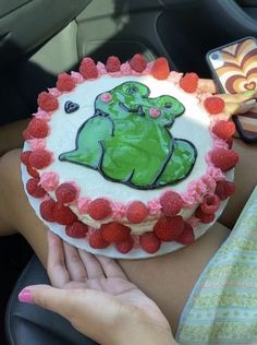 a person holding a cake with raspberries in the shape of a frog on it