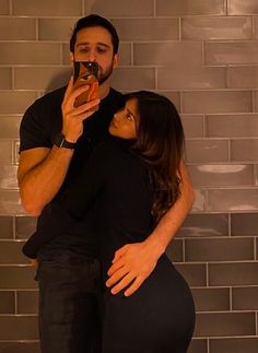 a man and woman taking a selfie in front of a brick wall