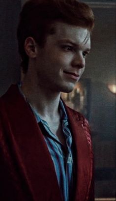 a young man with red hair wearing a blue shirt and jacket in a dark room