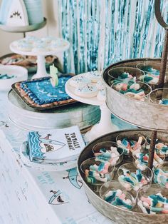 three trays filled with cupcakes and cookies on top of a blue table cloth