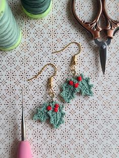 crocheted holly earrings with red berries and green leaves on them next to a pair of scissors