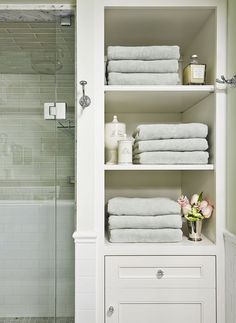 a bathroom with white shelves and towels on top of each shelf in front of the shower