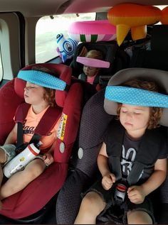 two young children sitting in the back of a car with head pillows on their heads