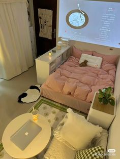 a bed with pink sheets and pillows in front of a projector screen on the wall