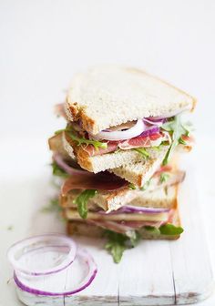 a sandwich with meat, lettuce and onions on a cutting board