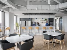 an office with tables and chairs in front of the counter, two people are standing at the bar