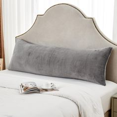 a white bed topped with a gray pillow next to a window