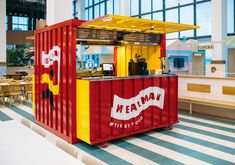 a red and yellow food cart sitting in the middle of a room next to tables