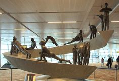 there are many statues on display in the airport lobby, including men laying on surfboards