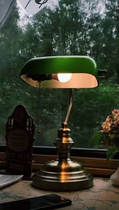 a green lamp sitting on top of a desk next to a window