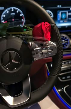 a red rose sitting on the steering wheel of a mercedes benz car with dashboard lights and gauges