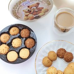 two plates with cookies on them next to a cup of coffee and a teddy bear cookie tin