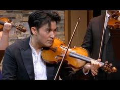 a young man playing the violin in front of other violinist's and orchestra members