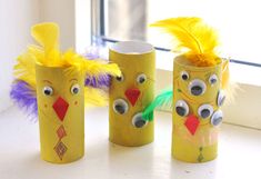 three toilet paper roll crafts with faces and feathers on the windowsill in front of a window