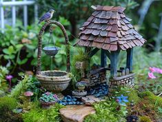 a bird is perched on top of a miniature house in the garden with plants and rocks