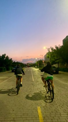 two bicyclists riding down the street at sunset