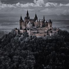 an old castle sits on top of a hill with trees in the foreground and clouds in the background