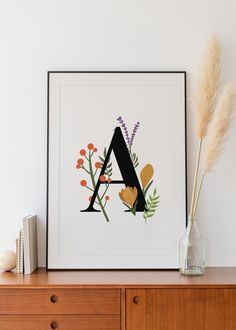 an art print with the letter a surrounded by wildflowers and leaves on a dresser