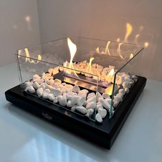 a glass fire pit sitting on top of a white table next to rocks and water