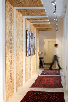 a person walking down a long hallway with wooden panels on the walls and rugs on the floor