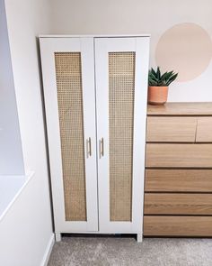 a white cabinet with wicker doors next to a wooden dresser and potted plant