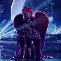 a woman sitting on top of a stage with an angel wings around her neck and legs