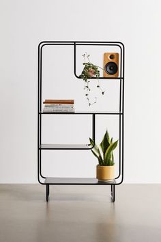 a shelf with books, plants and a camera sitting on it's side next to a potted plant