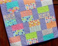 a purple quilt with multicolored squares and flowers on the front is hanging from a wooden fence